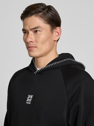 Männermodel trägt Regular Fit Hoodie aus reiner Baumwolle Modell 'DAROHOOD' von HUGO in Schwarz mit weißen Ziernähten, Nahaufnahme Oberkörper.