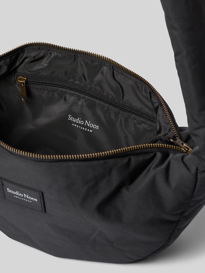 Produktfoto, schwarze Shoulder Bag mit Logo-Detail Modell 'Puffy' von Studio Noos, Reißverschluss, Schulterriemen, glatte Textur, 38x20x9 cm, Riemen 86 cm, Hauptfach innen sichtbar
