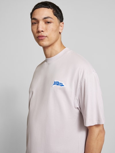 Męski model nosi Oversized T-Shirt aus reiner Baumwolle Modell 'Nohatio' od HUGO, efekt: jednolity kolor, aplikacja z metką, okrągły dekolt, krótki rękaw, prosty dół z rozcięciami po bokach, wykończenie: dżersej, materiał: czysta bawełna, kolor jasny, gładka faktura, zbliżenie na górną część ciała, ujęcie z przodu.