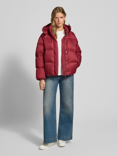 Modelka nosi Regular Fit Daunenjacke mit abnehmbarer Kapuze od Levi's® 300 w kolorze bordowym, białą koszulkę, niebieskie dżinsy, białe buty, gładka faktura, Ganzkörperansicht von vorne.