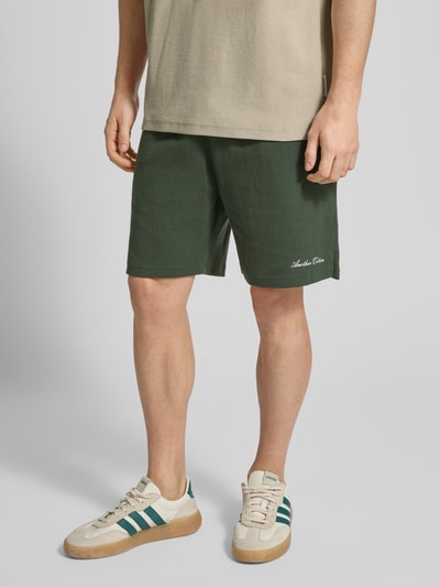 Männermodel trägt Shorts mit Logo-Print und Eingrifftaschen von ANOTHER COTTON LAB in Dunkelgrün, Baumwoll-Mix, Nahaufnahme Oberschenkel.