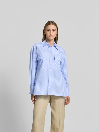 Frauenmodel trägt Relaxed Fit Hemdbluse aus Baumwolle von Joseph, hellblau-weiß gestreift, durchgehende Knopfleiste, Langärmelig, Ganzkörperansicht von vorne. Rückenlänge bei Größe 36: 83 cm, Ärmellänge: 58 cm, verlängerte Rückseite, glatte Struktur.