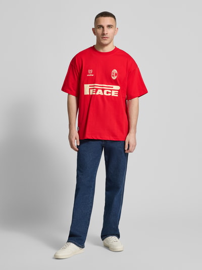 Männermodel trägt Regular Fit T-Shirt mit Logo-Print von ANOTHER COTTON LAB in Rot, Baumwolle, goldener Schriftzug, Ganzkörperansicht von vorne.