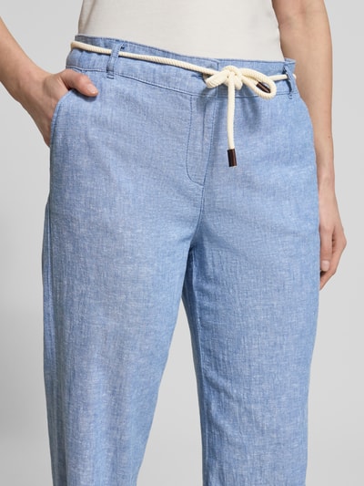 Kobieta nosi spodnie Hose aus Leinen-Baumwoll-Mix mit Bindegürtel od Christian Berg Woman, mieszanka lnu i bawełny, spodnie z szerokimi nogawkami, wiązany pasek, wpuszczane kieszenie, szerokość w rozmiarze 36: 41 cm, długość wewnętrzna nogawki w rozmiarze 36: 81 cm, jasnoniebieskie, tekstura lekko melanżowa, zbliżenie na biodra i talię, detal.