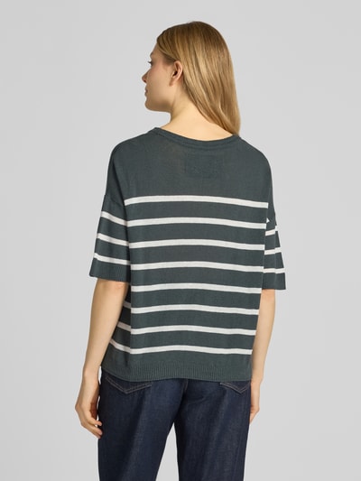 Frauenmodel trägt Relaxed Fit Pullover aus Leinen-Mix Modell 'STRIPE' von Armedangels mit Allover-Muster, Logo-Stitching, Rundhals, 1/2-Arm, Strick, dunkelgrün und weiß, gerippte Abschlüsse, Ganzkörperansicht Rückansicht.