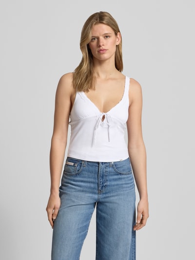 Vrouwenmodel draagt Slim Fit Top mit Spitzenbesatz van Guess Jeans in wit, elastische katoenmix met modal, kanten rand, sierstrik, mouwloos, V-hals, ruglengte bij maat S 26 cm, eenvoudige structuur, gladde textuur, voorkant volledige lichaamsopname.