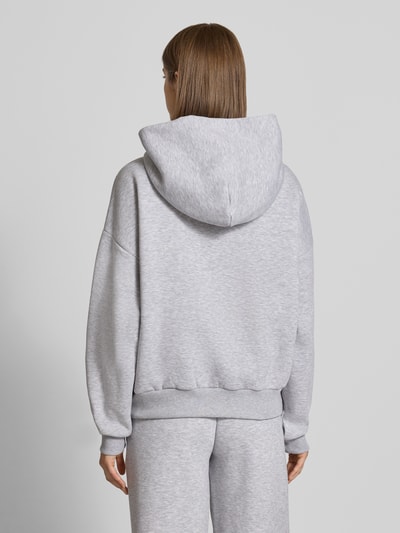 Frauenmodel trägt Relaxed Fit Basic Hoodie in grau melange von REVIEW, mieszanka bawełny, krój relaxed fit, kaptur, nadruk z logo, kieszeń kangurka, prążkowane wykończenia, Ganzkörperansicht Rückansicht
