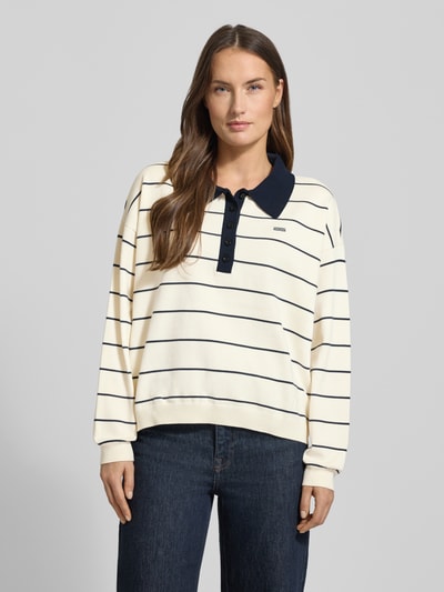 Kobiece model prezentuje Sweter z dzianiny z mieszanki wiskozy Model 'taige' od Gestuz, krój oversized, kołnierzyk polo, wyhaftowane logo, prążkowane wykończenia, długość tyłu 56 cm, długość rękawów 50 cm, białe tło z czarnymi paskami, widok całej sylwetki z przodu.