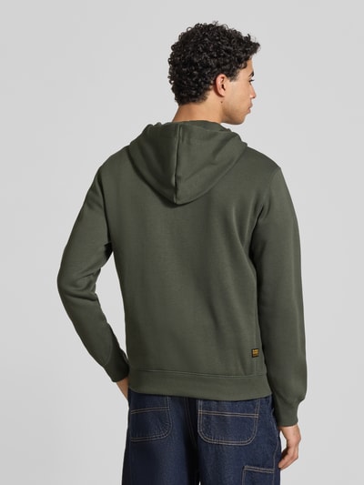 Männermodel trägt groene Heren Sweatjack 'Premium core' van G-Star Raw van katoenmix met opstaande kraag, capuchon, recht model, ruglengte 67 cm, mouwlengte 65 cm, steekzakken, gestikt logo, doorlopende ritssluiting, Ganzkörperansicht Rückansicht.