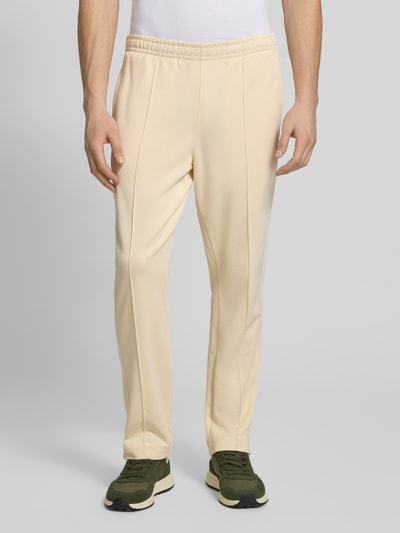 Männermodel trägt Regular Fit Sweatpants mit Baumwoll-Anteil von Lacoste in Beige, Material-Mix, unifarben, elastischer Bund, Galonstreifen, Ganzkörperansicht von vorne.