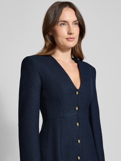 Vrouwenmodel draagt Tailliertes Freizeitkleid mit Viskose-Anteil Modell 'Kanegi-1' van HUGO in effen donkerblauw, getailleerde fit, bouclé, mini-lengte, diepe V-hals, knoopsluiting, lange mouwen, rechte zoom, materiaal-mix met viscose-aandeel, detailopname bovenlichaam.