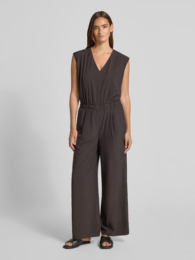 Kobiece modelka nosi kombinezon Relaxed Fit Jumpsuit mit V-Ausschnitt Modell 'Charlou' od Someday, elastyczna mieszanka materiałów, krój relaxed fit, dekolt w serek, bez rękawów, taliowany, wpuszczane kieszenie, długość tyłu w rozmiarze 36: 44 cm, szerokość w rozmiarze 36: 52 cm, całkowita długość w rozmiarze 36: 146 cm, długość wewnętrzna nogawki w rozmiarze 36: 71 cm, ciemny brąz, prosta tekstura, pełna sylwetka z przodu