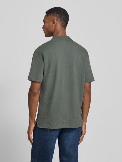 Männermodel trägt Relaxed Fit Poloshirt aus reiner Baumwolle von Marc O'Polo in Dunkelgrün mit Webstruktur, Ganzkörperansicht Rückansicht.