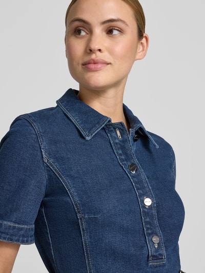 Frauenmodel trägt Knielanges Jeanskleid mit Gürtel von Marc Cain aus Baumwoll-Lyocell-Anteil in Dunkelblau, sichtbare Knopfleiste, Nahaufnahme Oberkörper.