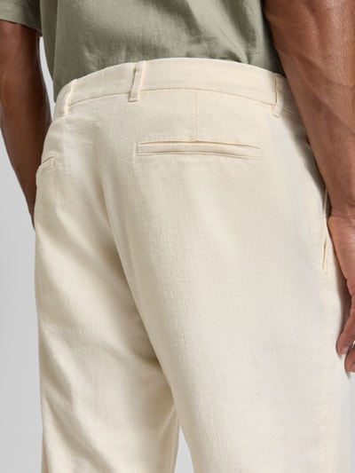 Männermodel trägt Relaxed Fit Bundfaltenhose aus Baumwoll-Mix mit Leinen-Anteil Modell 'LOUIS-W' von Strellson in Beige, Nahaufnahme Rückansicht. Material wirkt meliert, strukturierte Twill-Oberfläche mit Gürtelschlaufen und Label Patch.