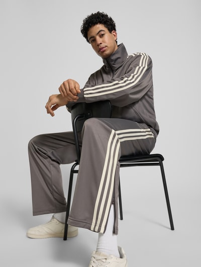 Männermodel trägt Straight Fit Sweatpants mit Logo-Stitching Modell 'Firebird' von adidas Originals in Grau mit Eingrifftaschen, Ganzkörperansicht von vorne.
