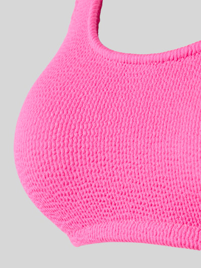 Vrouwenmodel draagt Bikini-Oberteil met Label-Detail Modell 'JUSTIN' van Banana Moon, felroze structuurstof, detailopname, materiaal-mix met stretch.