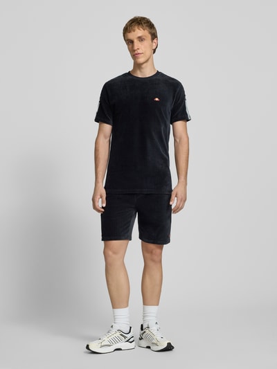 Männermodel trägt Herren T-Shirt mit Logo Modell 'MADORI' von Ellesse aus schwarzem Baumwoll-Mix mit Stretch-Anteil, Regular-Fit, Rundhalsausschnitt, dezente Streifenstruktur, Rückenlänge in Größe M 66 cm, Ganzkörperansicht von vorne.