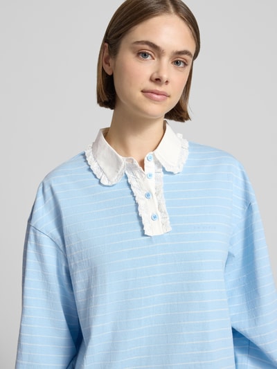 Frauenmodel trägt Relaxed Fit Poloshirt mit Label-Stitching Modell 'Jolina' von OH APRIL aus Reine Baumwolle, hellblau mit weißen Streifen, Spitzenbesatz und Knopfleiste, Nahaufnahme Oberkörper. Rückenlänge bei Größe S: 65 cm.