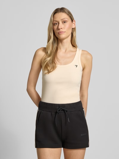 Frauenmodel trägt Slim Fit Top aus Viskose-Mix Modell 'Colette' von Guess Activewear in Beige mit Logo-Applikation, Nahaufnahme Oberkörper.