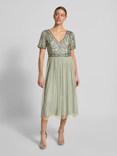 Frauenmodel trägt knielanges Kleid mit floralem Pailettenbesatz von LACE & BEADS in zartem Grün, Taillierte Passform, V-Ausschnitt, Mesh, kurzärmelig, Rückenlänge bei Größe S 100 cm, Brustweite 42 cm, Ärmellänge 19 cm, Ganzkörperansicht von vorne.