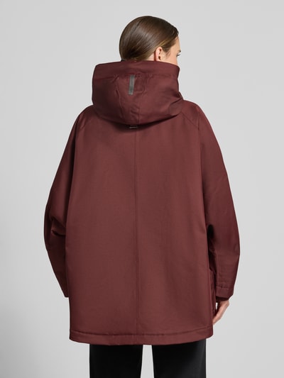 Frauenmodel trägt Relaxed Fit Mantel mit Kapuze Modell 'PURE' von g-lab in Dunkelrot, glatte Oberfläche, Rückenansicht, Detailaufnahme. Rückenlänge, Schulterbreite, Brustweite und Ärmellänge entsprechend Größe S. Mit Tunnelzug und Eingrifftaschen.