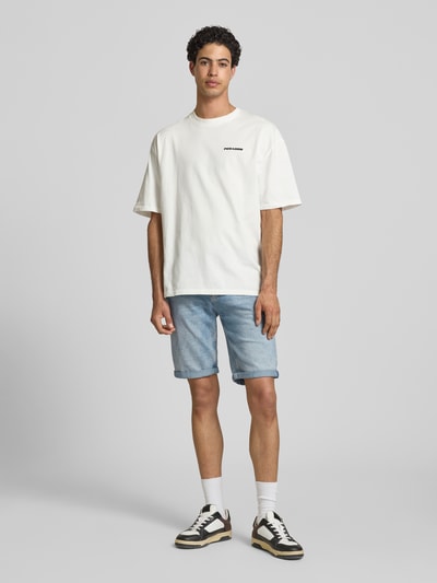 Männermodel trägt Regular Fit Jeansshorts aus Baumwoll-Mix Modell 'RONNIE' von Tommy Jeans in hellblauem Denim mit 5-Pocket-Design, Ganzkörperansicht von vorne.
