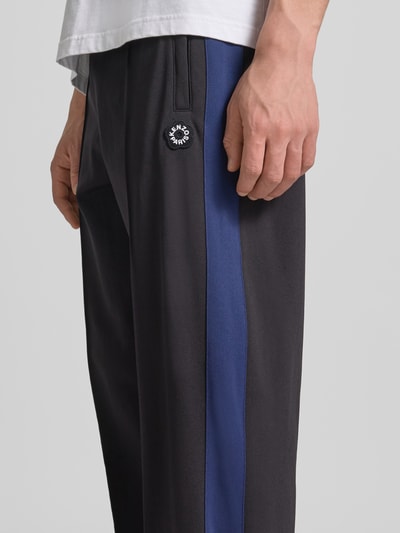 Männermodel trägt Sweatpants mit Logo-Stitching von Kenzo in Schwarz mit blauen Seitenstreifen aus reiner Baumwolle, Ziernähte, Nahaufnahme Oberkörper. Herren Sweatpants, Straight Fit, elastischer Bund, Innenbeinlänge 43 cm, Bundweite 79 cm.