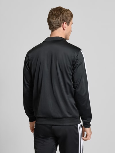 Männermodel trägt czarny 'Trainingsanzug mit Stretch-Anteil' von adidas Sportswear, mieszanka elastyczna, prosty krój, stójka, zamek błyskawiczny, elastyczne wykończenia i pas, wpuszczane kieszenie, detale z logo, szerokość w rozmiarze M: 39 cm, długość tyłu: 70 cm, szerokość ramion: 44 cm, długość rękawów: 65 cm, długość wewnętrzna nogawki: 73 cm, widok całej sylwetki z tyłu