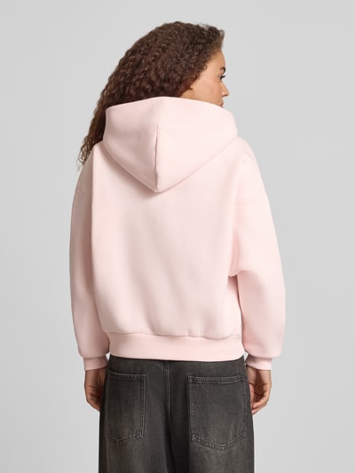 Männermodel trägt Relaxed Fit Sweatjacke mit Kapuze von REVIEW, bawełna, jasnoróżowa, logo-print, kieszenie kangurki, widok tył, Ganzkörperansicht Rückansicht.