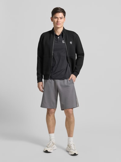 Männermodel trägt Regular Fit Poloshirt mit Logo von EA7 Emporio Armani, Schwarz und Grau, Material-Mix mit Stretch-Anteil, Ganzkörperansicht von vorne.