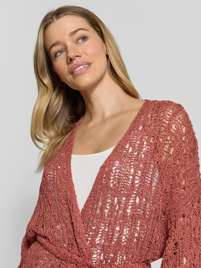 Vrouwenmodel draagt Strickjacke mit Bindegürtel und 3/4-Arm van Marc Cain, biologisch katoen, relaxed fit, open pasvorm, strikceintuur, 3/4-mouw, ruglengte maat 36: 74 cm, mouwlengte maat 36: 34 cm, structuur breipatroon in warme rozetint, detailopname bovenlichaam.