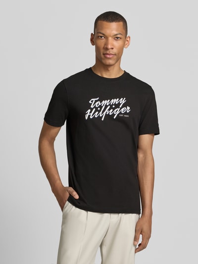 Männermodel trägt Regular Fit T-Shirt aus reiner Baumwolle von Tommy Hilfiger, schwarz, Label Print, unifarben, Jersey, Nahaufnahme Oberkörper.