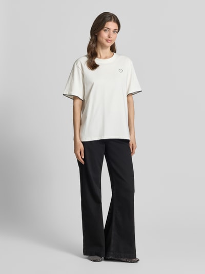 Frauenmodel trägt T-Shirt mit Rundhalsausschnitt und Stitchings von FREE/QUENT in Beige, lockerer Schnitt, schwarze Hose, Ganzkörperansicht von vorne.