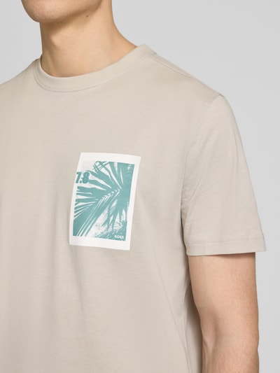 Männermodel trägt Regular Fit T-Shirt aus reiner Baumwolle Modell 'TE_BOARD' von BOSS Orange in Beige mit Foto-Print und Label, Nahaufnahme Oberkörper.