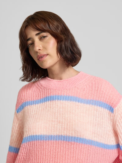 Frauenmodel trägt Strickpullover aus Alpaka-Mix mit Rundhalsausschnitt von Closed in Rosa mit blauen Streifen, relaxter Allover-Look, Nahaufnahme Oberkörper.