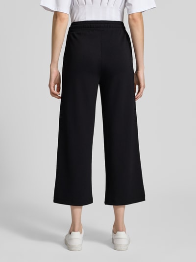 Kobieta nosi spodnie dresowe Wide Fit Sweatpants in verkürzter Passform Modell 'Banu' od Soyaconcept, elastyczna mieszanka materiałów z domieszką modalu, szeroki krój, skrócona długość, czarny kolor, pas z tunelem, zdjęcie całej sylwetki z tyłu.