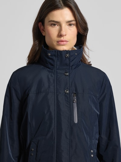 Frauenmodel trägt Funktionsjacke mit Brusttasche von Gil Bret in Dunkelblau mit Stehkragen und Reißverschluss, Nahaufnahme Oberkörper, taillierte Passform, Kapuze, Tunnelzug, Rückenlänge 74 cm, Schulterbreite 41 cm, Brustweite 47 cm, Ärmellänge 65 cm.