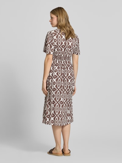 Vrouwenmodel draagt A-lijn midijurk van pure viscose model 'TALA' van Pieces met all-over patroon, elastische taille, rechte zoom, midi-lengte, korte mouw, V-hals, korte knoopsluiting, geheel bruine en witte kleuren, structuur glad, rugaanzicht full-body.