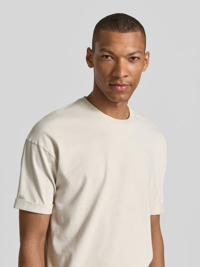 Männermodel trägt T-Shirt mit Ärmelaufschlag und Rundhalsausschnitt von Drykorn aus Reine Baumwolle Regular-Fit in Beige, Nahaufnahme Oberkörper.