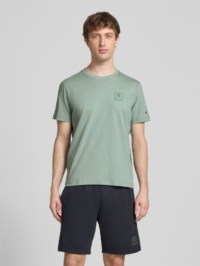 Männermodel trägt T-Shirt mit Logo und Rundhalsausschnitt von CHAMPION in Grün, Reine Baumwolle, Regular-Fit, Rückenlänge 68 cm bei Größe M, Ganzkörperansicht von vorne.