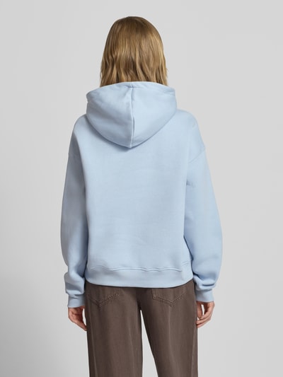 Modelka nosi Regular Fit Hoodie mit Känguru-Tasche Modell 'Iconic' von Gina Tricot w jasnoniebieskim kolorze, bawełniany miks, elastyczne wykończenia, widok całej sylwetki z tyłu.