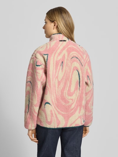 Modelka nosi kurtkę z polaru 'Fleecejacke im Allover-Look mit Stehkragen' od PEAK PERFORMANCE, krój regular fit, stójka, wzór na całej powierzchni, zamek błyskawiczny, długość tyłu w rozmiarze S: 65 cm, szerokość ramion w rozmiarze S: 52 cm, szerokość klatki piersiowej w rozmiarze S: 53 cm, długość rękawów w rozmiarze S: 56 cm, jasnoróżowe i kremowe odcienie, miękka tekstura, widok całej sylwetki z tyłu.