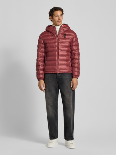 Männermodel trägt Steppjacke mit Zweiwege-Reißverschluss Modell 'CHARLES' von Blauer USA in Rot, glatte Oberfläche, Ganzkörperansicht von vorne. Regular Fit, Kapuze, Reißverschlusstaschen, Label-Detail, Maße für Größe M.