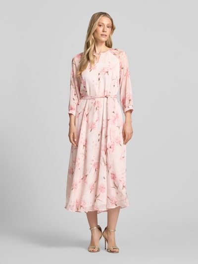Modelka kobieca nosi Midikleid mit Bindegürtel od More & More, jasnoróżowe z kwiatowym wzorem, krój taliowany, dekolt okrągły z cut out, pasek wiązany, rękaw 3/4, tylny dekolt typu łezka, zamek z tyłu, długość tyłu w rozmiarze 36: 128 cm, szerokość w rozmiarze 36: 42 cm, długość rękawa w rozmiarze 36: 58 cm, całość z przodu, widok całopostaciowy