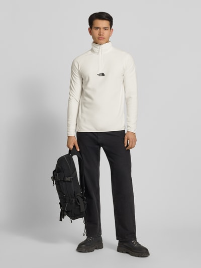 Männermodel trägt Fleecepullover mit Reißverschluss Modell 'GLACIER' von The North Face in Weiß, Regular-Fit, Stehkragen, Label-Stitching, schwarze Hose, Ganzkörperansicht von vorne. Rückenlänge bei Größe M: 70 cm, Ärmellänge: 67 cm.