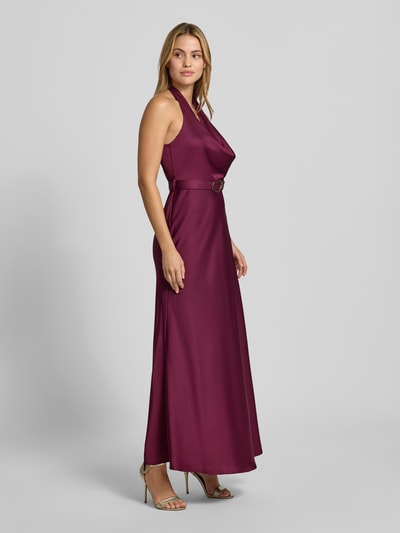 Frauenmodel trägt Abendkleid mit Neckholder von Rinascimento in dunklem Violett, taillierte Passform, Stoffgürtel, Maxikleid, Ganzkörperansicht von vorne.