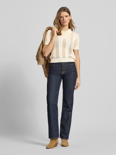 Frauenmodel trägt Slim Fit Poloshirt in Strick-Optik Modell 'Ajour' von Review in Creme mit Loch-Optik, Kurzarm, Jeans, Ganzkörperansicht von vorne.