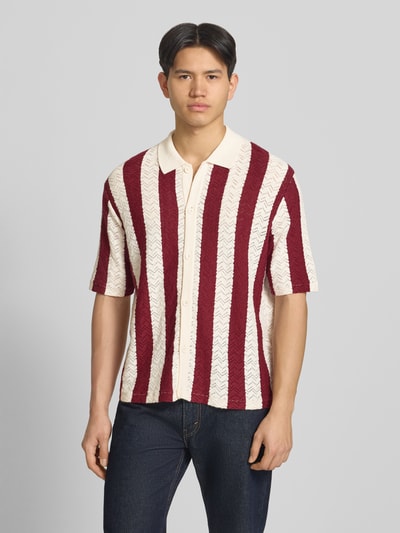 Männermodel trägt Regular Fit Poloshirt mit Knopfleiste Modell 'TYLER' von Jack & Jones aus Baumwoll-Mix mit roten und weißen Streifen, 1/2-Arm, Ganzkörperansicht von vorne.