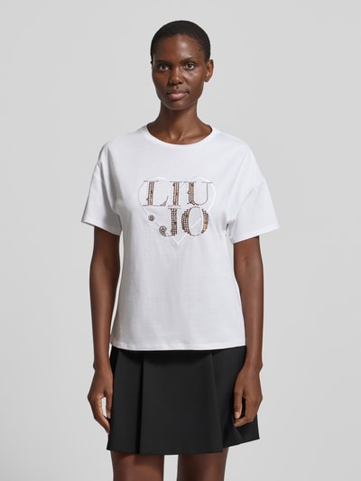 Vrouwenmodel draagt Regular Fit T-shirt met strass-steentjes van Liu Jo White, puur katoen, logodetail, ronde hals, ruglengte maat S 60 cm. Ganzkörperansicht van voren.